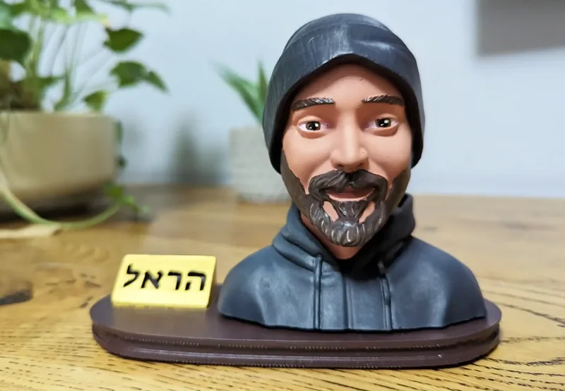 פסלון פורטרט של גבר עם כובע גרב וקפוצ׳ון, ושלט שם חרוט